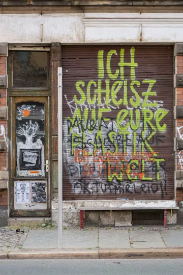 Auf dem heruntergelassenen Rolläden eines Geschäfts in der Merseburger Straße in Leipzig steht der Text, »Ich scheisse auf eure Plastikwelt«.