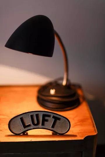 Eine aufbereitete Tischlampe beleuchtet ein emailliertes Schild mit der Aufschrift »Luft«